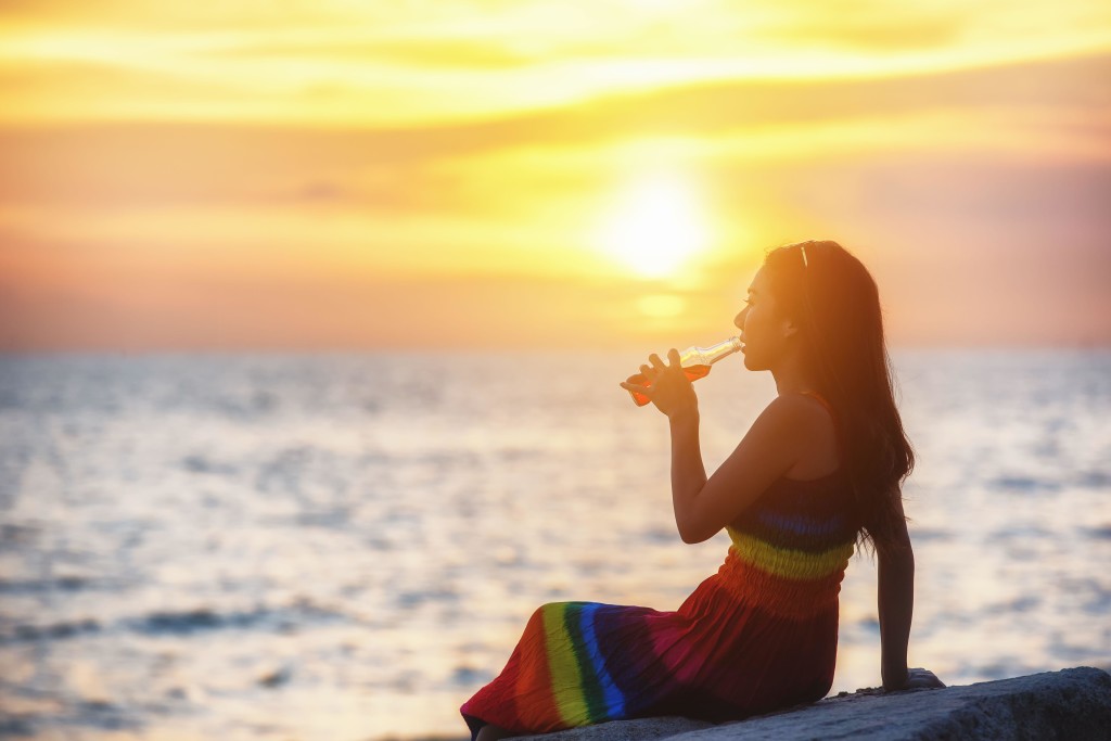 Young Asian Woman enjoying a Bottle of Red wine on the beach